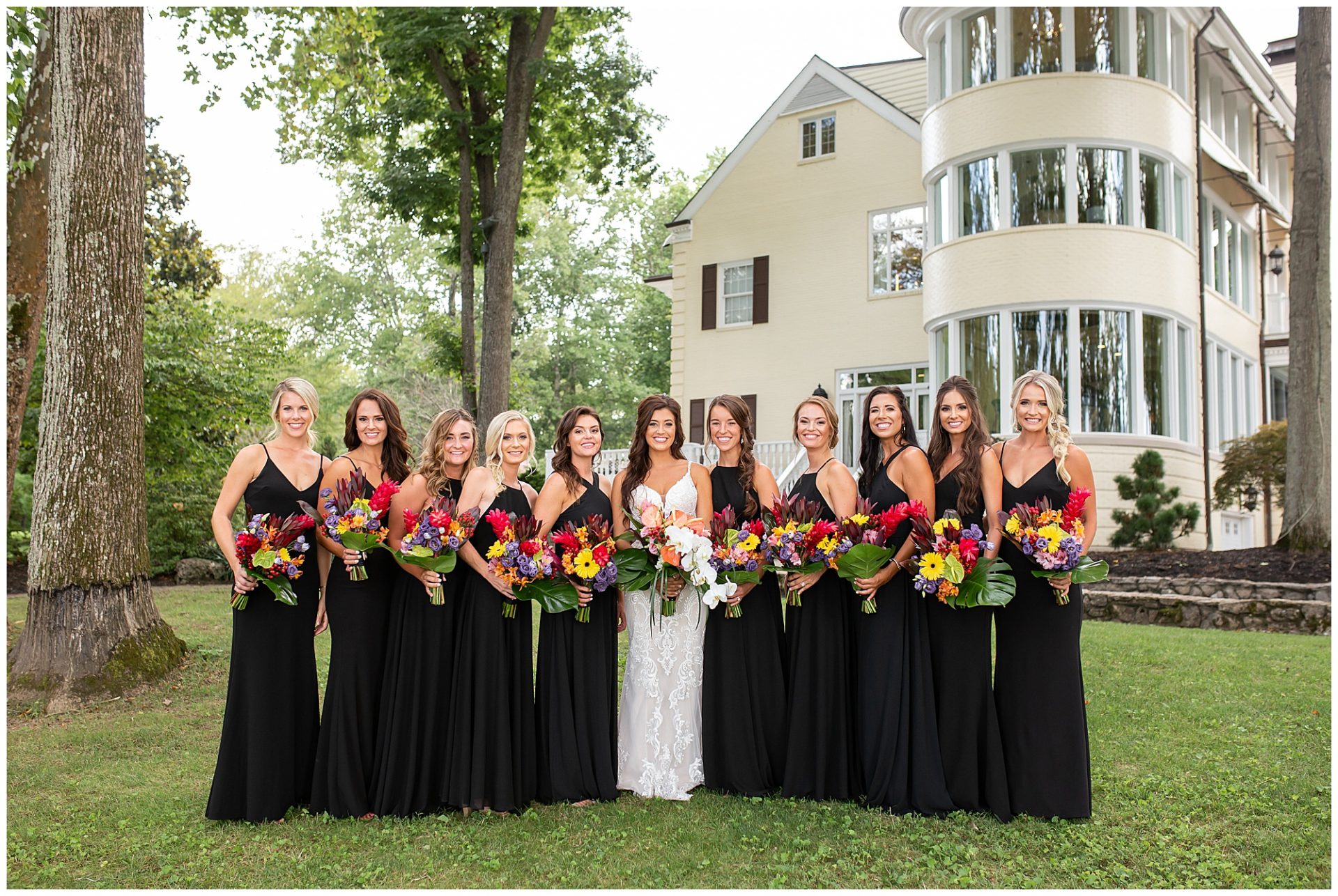 Bridesmaids in black gowns and colorful tropical floral bouquets at Cherokee Dock in Nashville